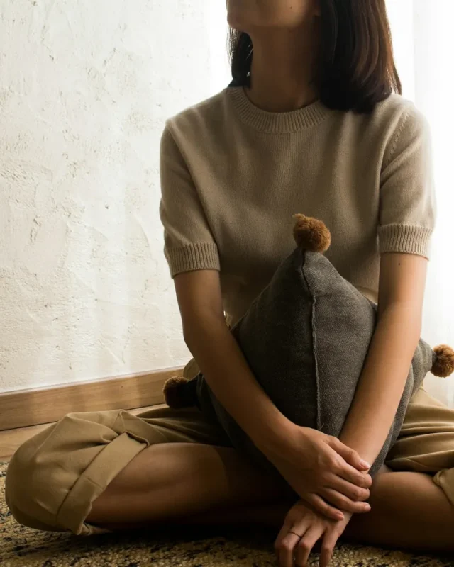 Người phụ nữ ngồi ôm gối bên rèm cửa, lắng nghe cảm xúc bên trong