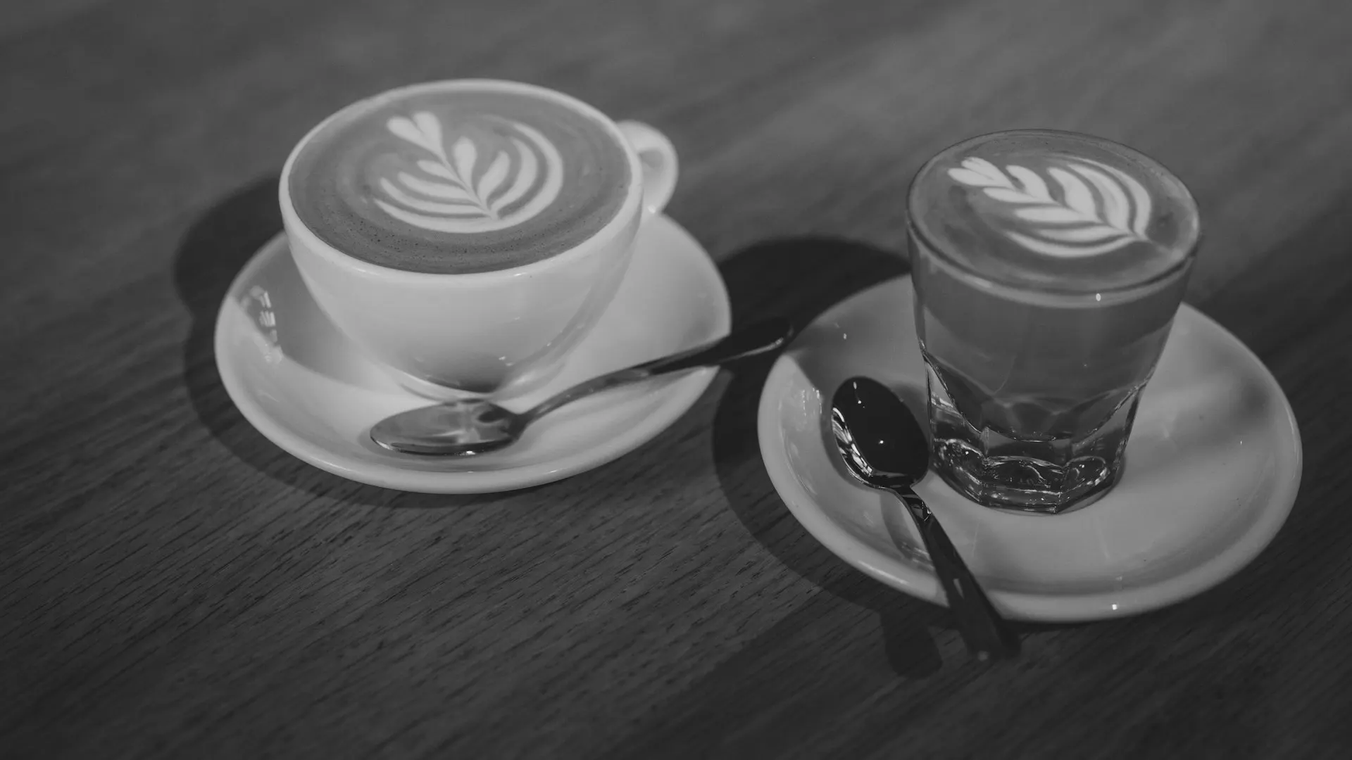Hai cốc cà phê nghệ thuật đặt trên đĩa sứ trắng và mặt bàn gỗ